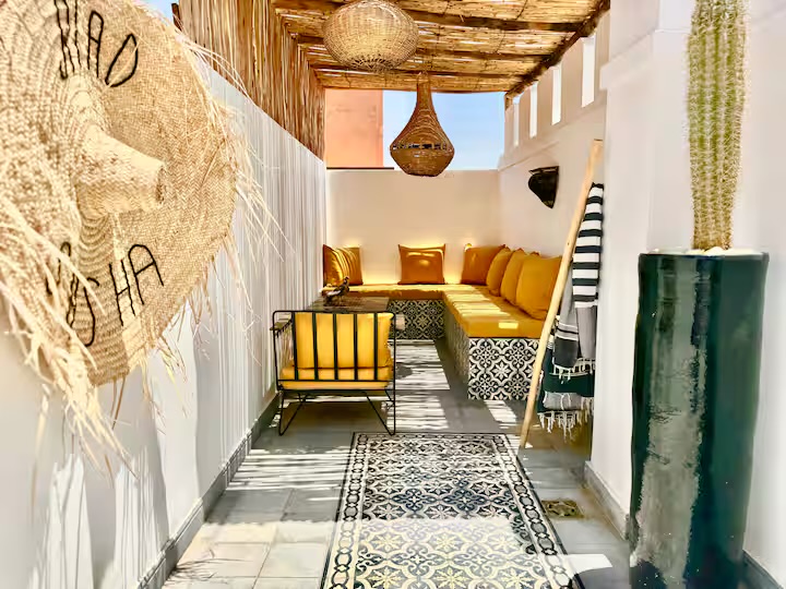 Salon couvert de la terrasse de Riad Sasha, banquette à coussins jaunes sous une pergola en roseau